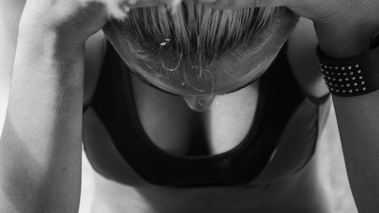 Black and white photo of a woman in sports attire reflecting in thought.